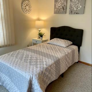 A cozy and well-decorated bedroom featuring a single bed with a soft quilt, accompanied by stylish wall art and a bedside lamp.