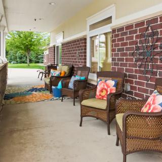A cozy outdoor patio with wicker chairs adorned with colorful pillows, set against a brick wall.