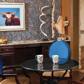 A cozy interior space featuring a small round table with two patterned mugs, surrounded by chairs. The background showcases decorative art and sculptures.