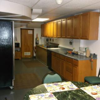 A kitchen interior with wooden cabinets, a black refrigerator, and a dining area featuring a table and chairs.