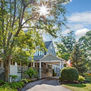 A picturesque house with sunlight filtering through trees, surrounded by a lush garden and driveway.