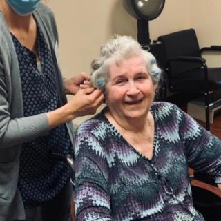 An elderly woman smiling while getting her hair styled at a salon.