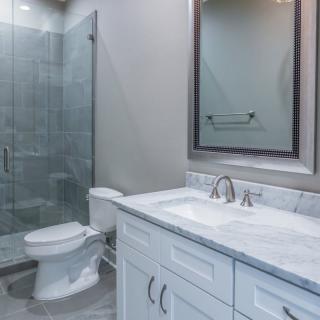 A modern bathroom with a glass shower, sink, and white cabinetry.