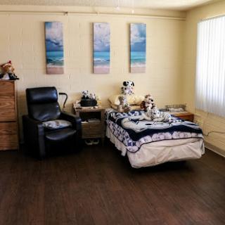 A cozy and simple bedroom featuring a bed, a reclining chair, and decorative wall art.