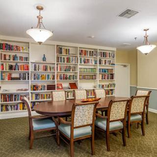 A cozy library reading room featuring a long wooden table surrounded by chairs, with bookshelves lining the walls.