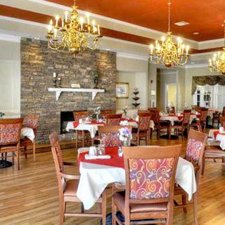 A cozy restaurant interior featuring elegant chandeliers, neatly arranged tables and chairs, and a stone fireplace.