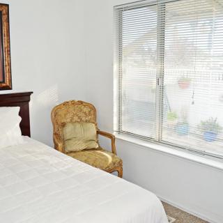 A cozy bedroom featuring a bed with white linens, an upholstered chair by the window, and a bright atmosphere.