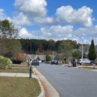 A suburban street lined with houses and greenery under a partly cloudy sky.