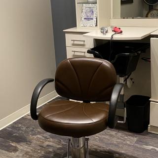 A salon chair in front of a styling station, complete with a mirror and sink.