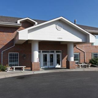 The image shows a brick building with a prominent entrance, featuring large columns and glass doors.