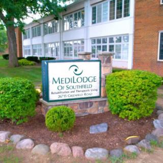A nursing home building with a Medilodge sign surrounded by well-maintained landscaping.
