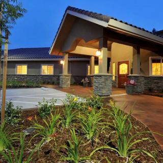 A modern residential house with illuminated exterior and landscaped garden in the evening.