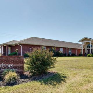 A brick building with a sign and surrounding grass and bushes under a clear sky.