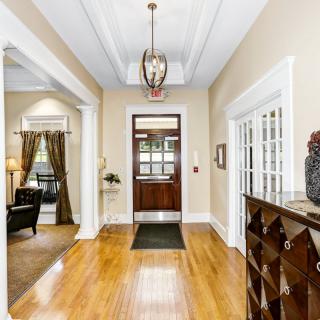 A bright and welcoming hallway with wooden flooring, a chandelier, and elegant decor.
