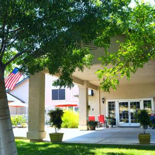 The entrance to a building with a patio, surrounded by trees and an American flag visible in the background.