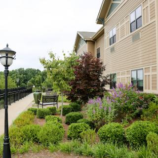 A well-maintained garden area beside a residential building, featuring lush greenery and a charming pathway.