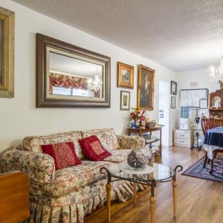 A cozy living room with a floral sofa and various artworks, featuring a wooden floor and a central coffee table.