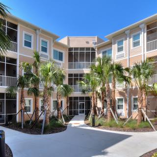 A modern apartment building surrounded by palm trees under a clear blue sky.