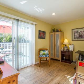 A cozy home office with wooden flooring and a sliding door leading to a patio, featuring a desk, chair, and ample natural light.