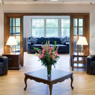 A cozy living room with elegant furniture, featuring a coffee table adorned with fresh flowers, surrounded by sofas and illuminated by two lamps.