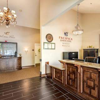 A warmly lit hotel reception area featuring a wooden counter, chandelier, and comfortable seating.