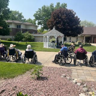 A serene outdoor gathering for seniors in wheelchairs, enjoying a sunny day in the garden.