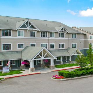 A three-story residential building with a landscaped entrance and clear blue sky.