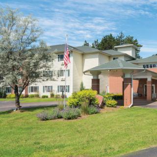 A residential building with a well-maintained lawn and surrounding trees under a clear blue sky.