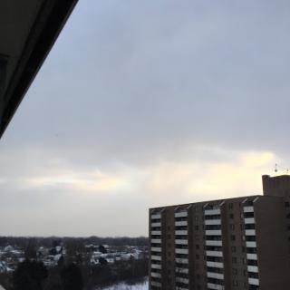 An overcast sky viewed from an apartment balcony, with a glimpse of snowy rooftops in the background.