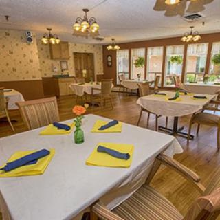 A cozy dining area with neatly arranged tables and chairs, featuring colorful napkins and warm lighting.