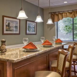 A cozy dining area with a bar counter, featuring pendant lights, framed artwork, and neatly arranged place settings.