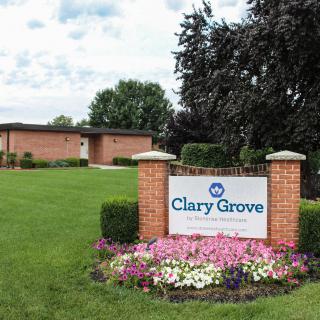 A landscaped area featuring a sign for Clary Grove, surrounded by flowers and greenery, with a building in the background.