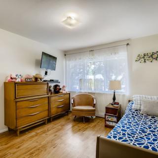 A cozy bedroom featuring a dresser, wall-mounted television, and a single bed against the wall.