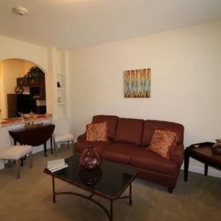 A cozy living room with a brown sofa, coffee table, and a small dining area in the background.