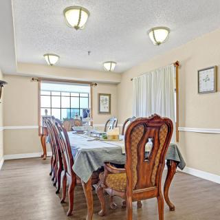 A well-lit dining room with a large wooden table and chairs, featuring elegant light fixtures and wood flooring.