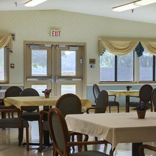 A well-lit dining room with tables and chairs, featuring large windows and natural lighting.