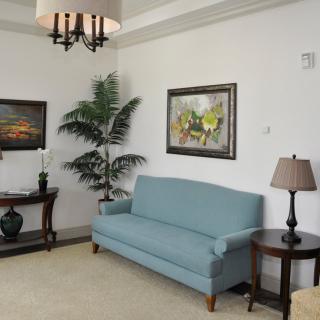 A cozy living room with a blue sofa, side tables with lamps, decorative paintings, and an indoor plant.