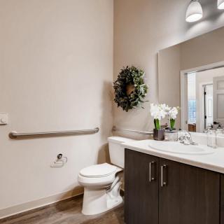 A modern bathroom featuring a toilet, sink with dark cabinetry, and a large mirror accented by a wreath and potted flowers.