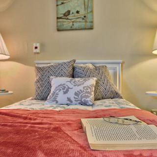 A cozy bedroom setup with a neatly made bed featuring patterned pillows, two bedside lamps, and an open book on the blanket.