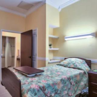 A cozy bedroom with a single bed featuring floral bedding, illuminated by a wall lamp beside an open door.