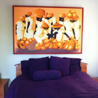 A bedroom with purple bedding and a vibrant painting depicting figures in orange.