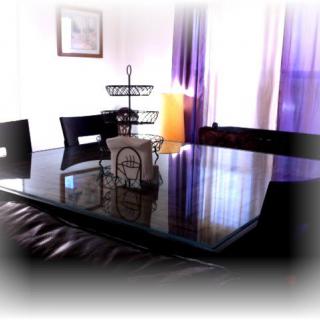 A dining room with a glass-top table and modern decor, accented by purple curtains and soft lighting.