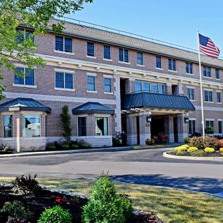 A three-story hotel building with a landscaped entrance and an American flag flying in front.