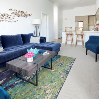 Modern living room with a blue sofa, stylish armchair, and open layout leading to the kitchen.