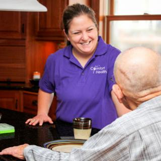 A caregiver engages in a warm conversation with an elderly person in a cozy kitchen setting.