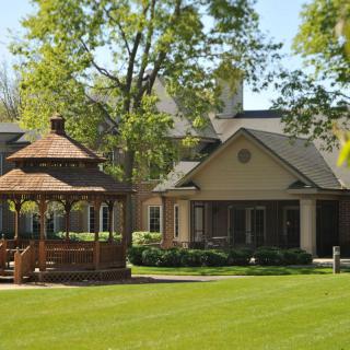 A charming house with a wooden gazebo surrounded by a lush green lawn and trees.