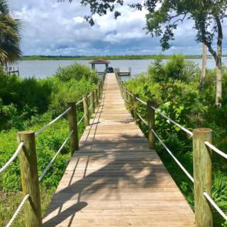 A serene wooden dock leading to a lake, surrounded by lush greenery and a cloudy sky.