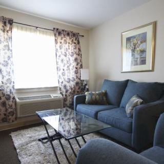 A cozy living room with comfortable sofas, a glass coffee table, patterned curtains, and wall artwork.