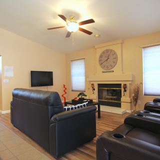 A cozy living room featuring leather sofas, a fireplace, mounted television, and a ceiling fan.