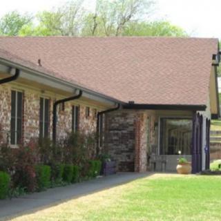 A one-story house with a brick exterior and a sloped roof, surrounded by a grassy lawn.